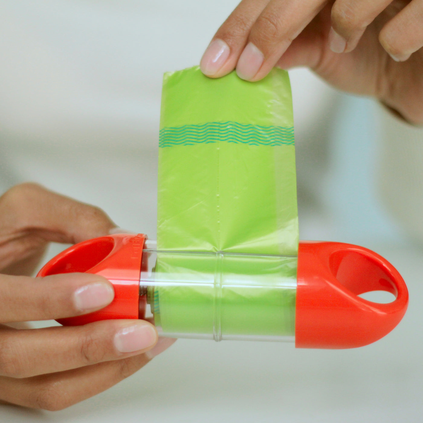 Dispensing a biodegradable poop bag from an orange LOOP poop bag holder.#color_orange